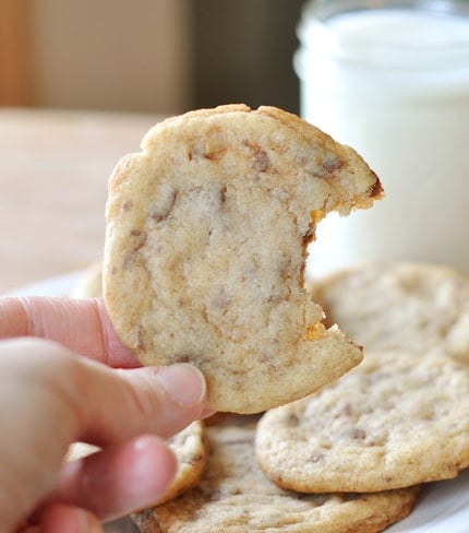 A hand holding a toffee studded cookie with a bite taken out of it.