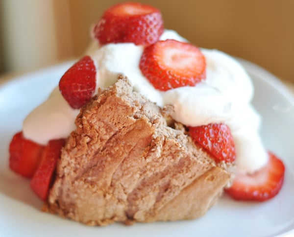 Slice of angel food cake with whipped cream and sliced strawberries on a white plate.
