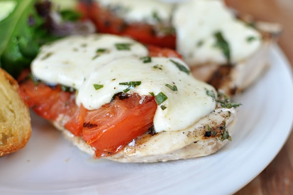 Grilled caprese chicken breasts with sliced tomato and melted cheese on a white plate.