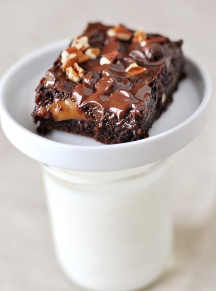 A white plate with a caramel topped brownie on it, with the plate sitting on top of a mason jar full of milk.