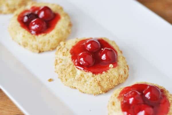 cheesecake cookies with a cherry center lined up on a white plate