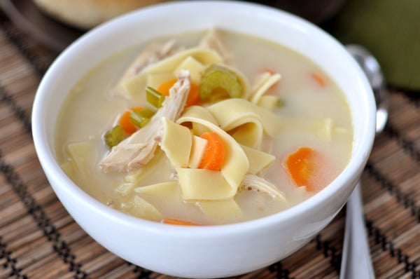 Top down view of a white bowl full of chicken noodle soup with sliced carrots and celery.