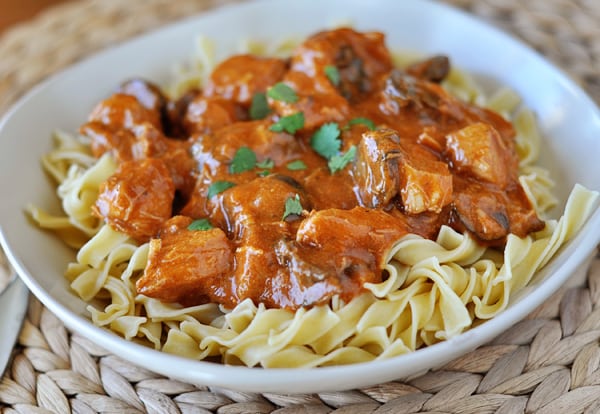 White bowl of cooked noodles with cubes of chicken and an orange paprika sauce.