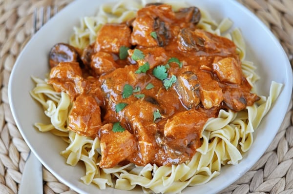 Top view of a white bowl with cooked noodles and cubed chicken smothered in an orange paprika sauce.