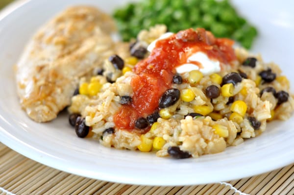 white plate with a large serving of rice with black beans and corn and topped with salsa, next to a chicken breast and green peas
