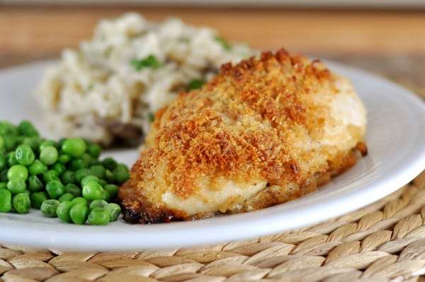 A white plate with green peas, mashed potatoes, and a crispy coated chicken breast.