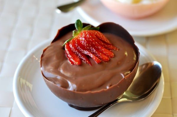 Round chocolate cup filled with chocolate pudding and topped with sliced strawberries.