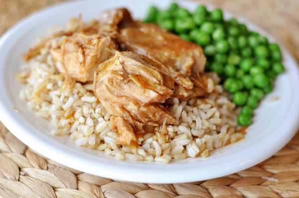 a white plate with brown rice, shredded pork on top of the rice, and green peas next to the rice