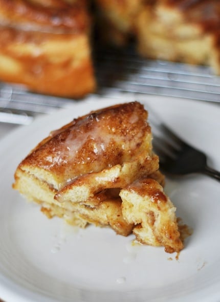 A pie shaped piece cut out of a giant cinnamon roll on a white plate.