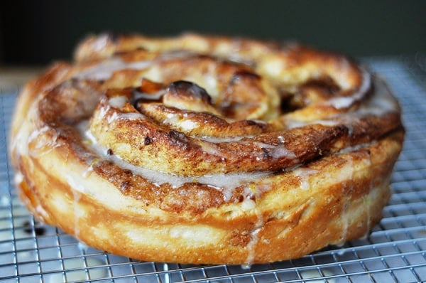 A giant frosted cinnamon roll on a cooling rack.