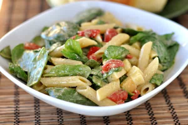 White dish with penne, spinach, mozzarella, and tomato salad.