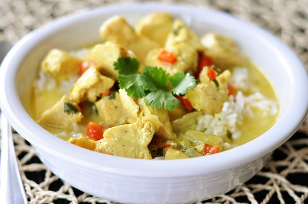 A white bowl of chicken curry soup over white rice.