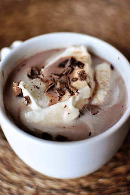 Top view of a white mug full of hot chocolate topped with whipped cream and bits of shaved chocolate.