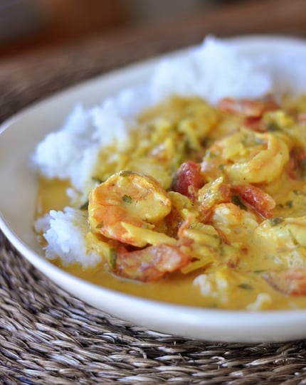 A white bowl with white rice topped with a shrimp curry tomato mixture.