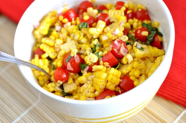 White bowl with a corn, tomato, and basil salad.