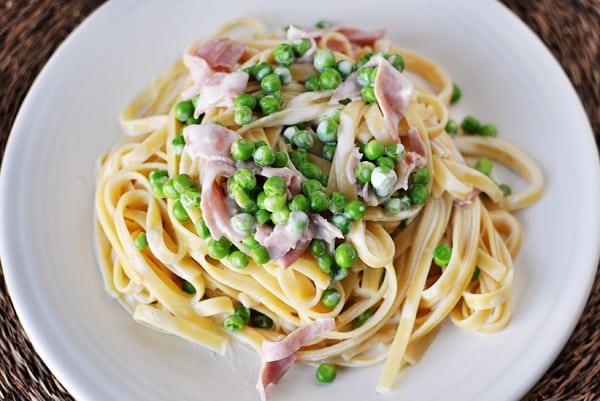 Top view of a white plate with creamy fettuccine topped with chopped ham and green peas.