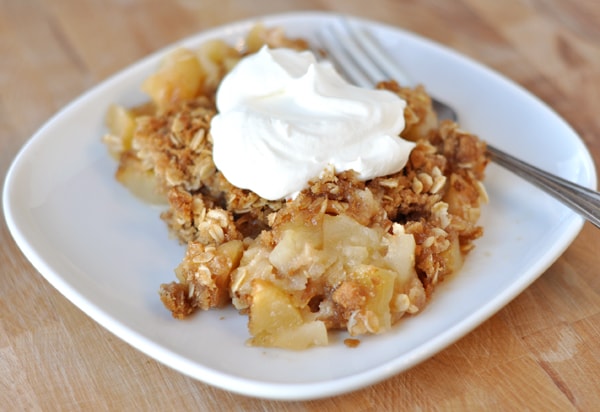 a white plate with baked apple crisp topped with whipped cream