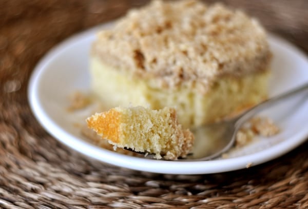 A piece of crumb cake on a white plate with a bite taken out.