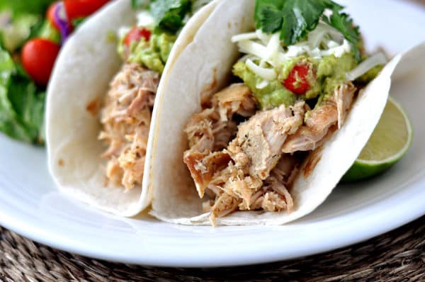 soft shell tacos filled with pork and toppings all on a white plate