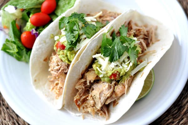 Top view of two soft shell tacos filled with pork and toppings all on a white plate.