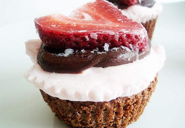 Chocolate cupcake with whipped cream, chocolate sauce, and a sliced strawberry.