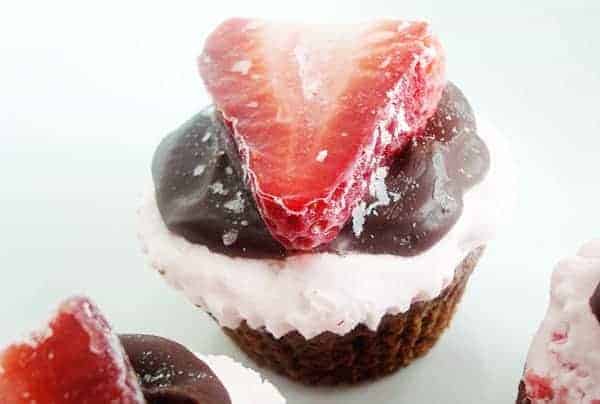 Chocolate cupcake with whipped cream, chocolate, and a sliced strawberry on top.