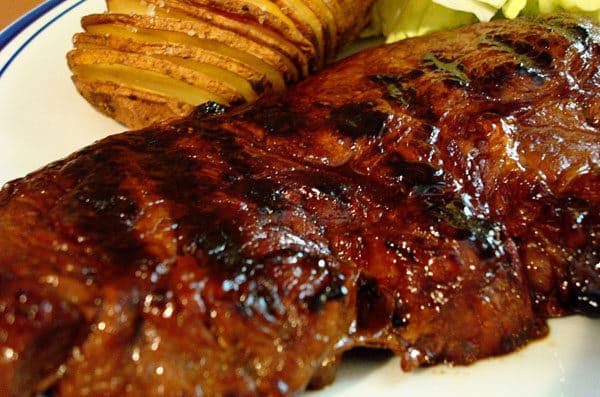 Grilled steak and a sliced baked potato on a white plate.