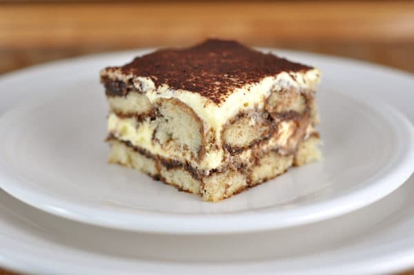 Piece of cocoa dusted tiramisu on a white plate.