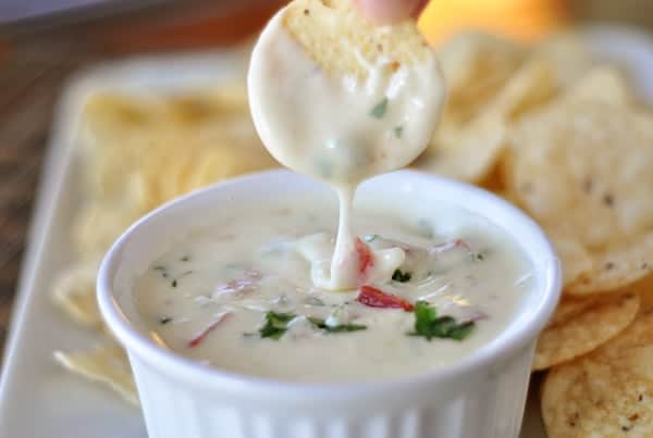 White ramekin with queso blanco dip and a cracker over the top that has just been dipped in it.