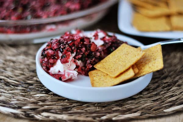 A small white dish with cream cheese and a chunky cranberry mixture on the top, and 4 crackers on the side of the dip. 