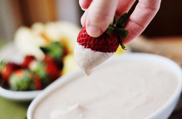 Half-dipped strawberry being held over a white bowl of fruit dip.