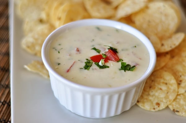 White ramekin with queso blanco dip on a tray with tortilla chips.