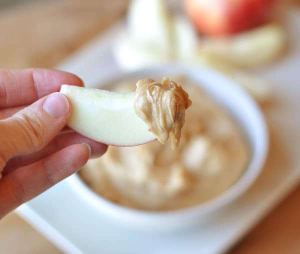 apple slice with dip on the end over the top of a white bowl of dip