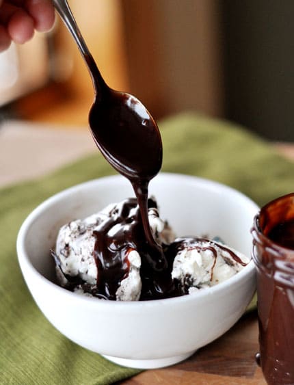 White bowl of ice dream with a spoon drizzling hot fudge sauce on top.