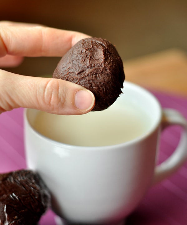A hand holding a truffle hot chocolate ball over a white mug filled with milk.