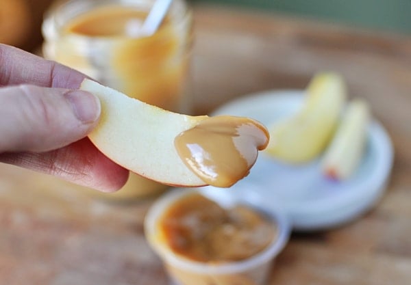 Someone holding a slice of apple with dulce de leche dipped on one end of the apple slice.