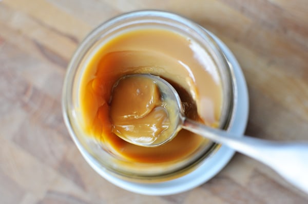 Top view of a spoon taking out a bite of dulce de leche from a glass mason jar.