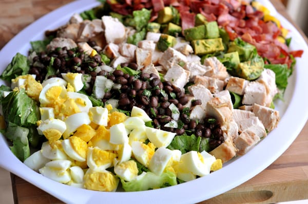 Chopped egg, black beans, chicken, bacon, and avocado on a white platter.