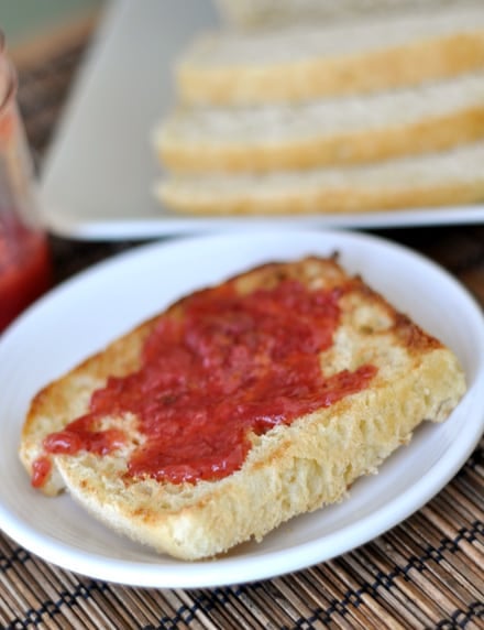 Toasted slice of english muffin with jam on a white plate.