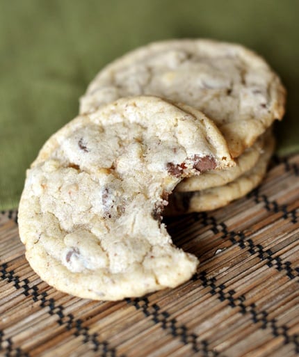 A stack of hazelnut cookies with one in front of the stack with a bite taken out.