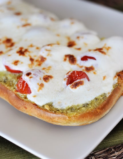 Slice of foccacia bread with pesto, tomatoes, and melted creme fraiche on top.
