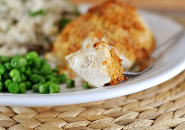 a white plate with a crispy coated chicken breast next to green peas