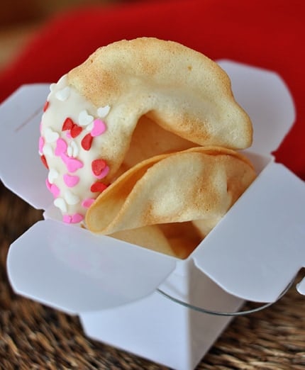 A white paper container full of cooked homemade fortune cookies.