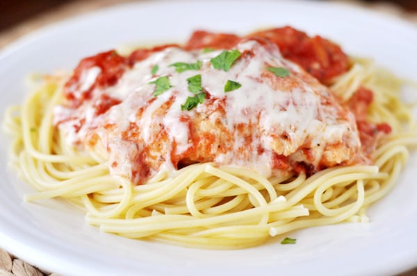 Chicken parmesan with melted cheese over a bed of cooked noodles on a white plate.