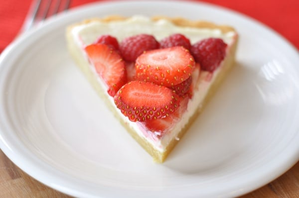 A triangle slice of fruit pizza on a white plate.