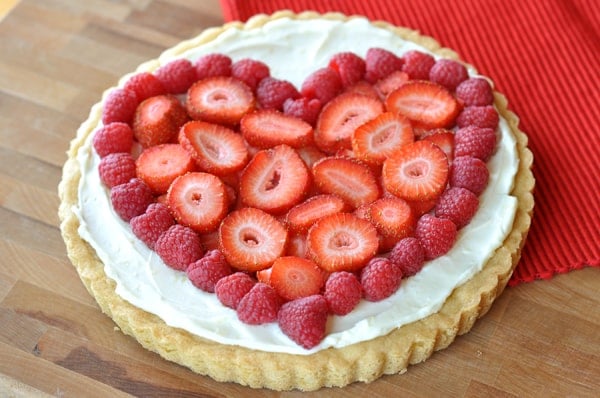 A sugar cookie crust with vanilla frosting and strawberries and raspberries on the top in the shape of a heart.
