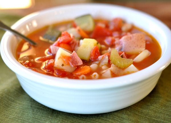 White bowl with red minestrone soup filled with vegetables and pasta.