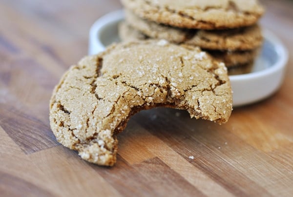 Ginger cookie with a bite taken out of it in front of a stack of ginger cookies.