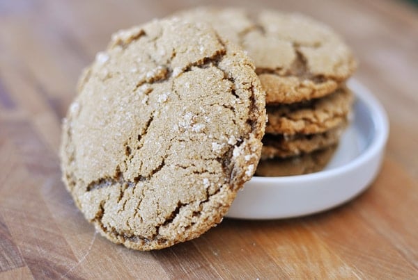 Four stacked ginger cookies in a white ramekin with another cookie leaning up against the side.