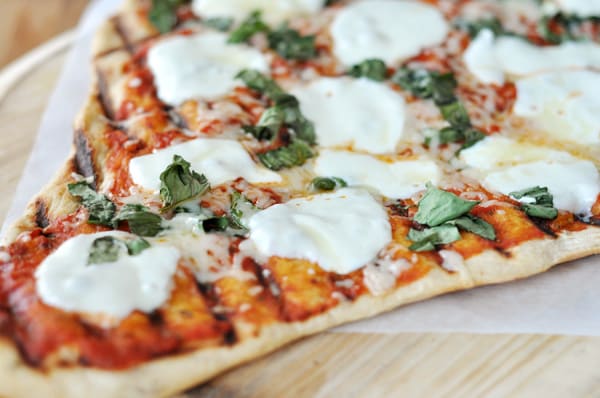 A triangle shaped grilled pizza with red sauce, melted mozzarella circles, and herbs.